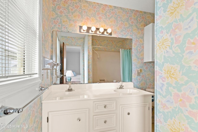 bathroom with a sink, a shower with curtain, double vanity, and wallpapered walls