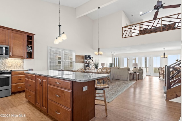 kitchen featuring a breakfast bar, light wood-style flooring, a ceiling fan, a center island, and appliances with stainless steel finishes