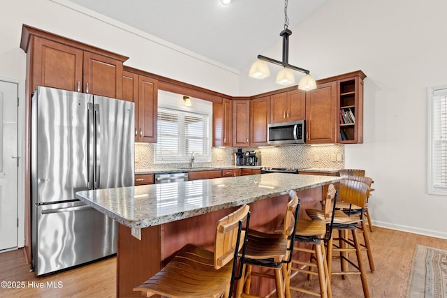 kitchen featuring light wood finished floors, lofted ceiling, appliances with stainless steel finishes, a kitchen bar, and backsplash