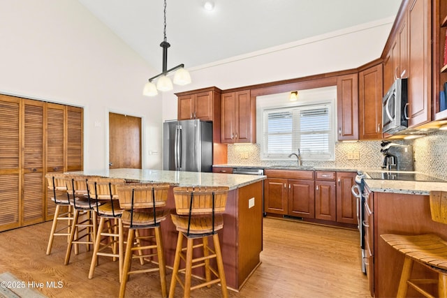 kitchen with a kitchen island, a sink, appliances with stainless steel finishes, a kitchen breakfast bar, and light wood-type flooring