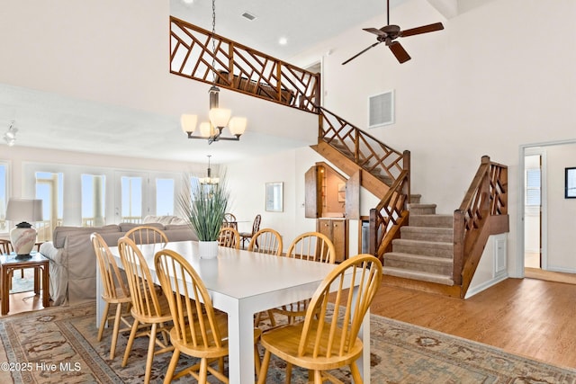 dining space with visible vents, wood finished floors, a towering ceiling, and stairway