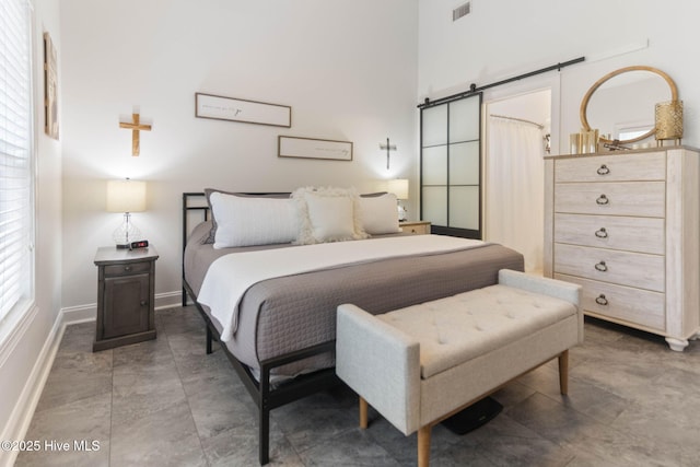 bedroom with a barn door, a high ceiling, baseboards, and visible vents