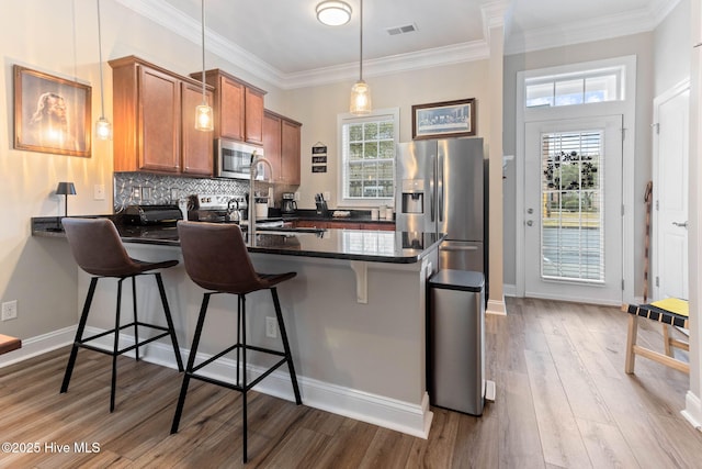 kitchen featuring visible vents, decorative backsplash, brown cabinets, appliances with stainless steel finishes, and a peninsula