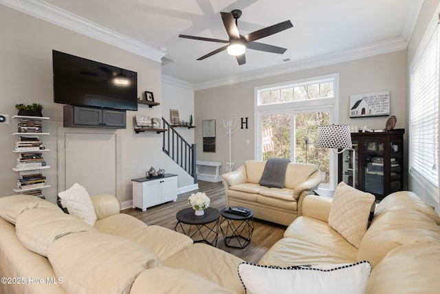 living area with stairway, a healthy amount of sunlight, crown molding, and wood finished floors