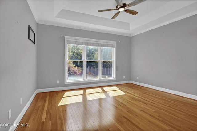 empty room with a tray ceiling, baseboards, and hardwood / wood-style flooring