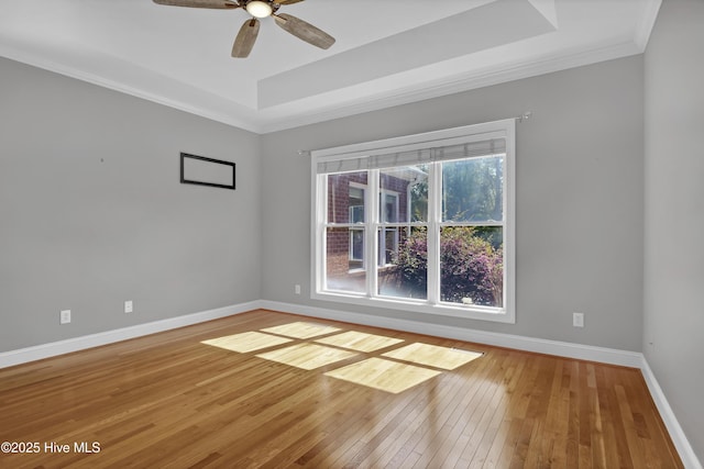 spare room featuring baseboards, a raised ceiling, hardwood / wood-style floors, and ornamental molding