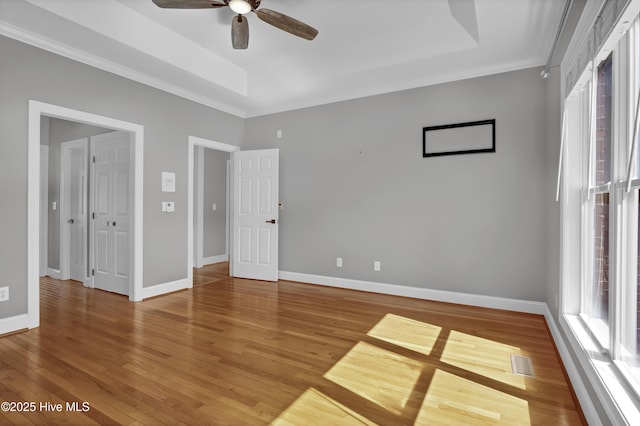 unfurnished bedroom featuring visible vents, a tray ceiling, wood finished floors, crown molding, and baseboards