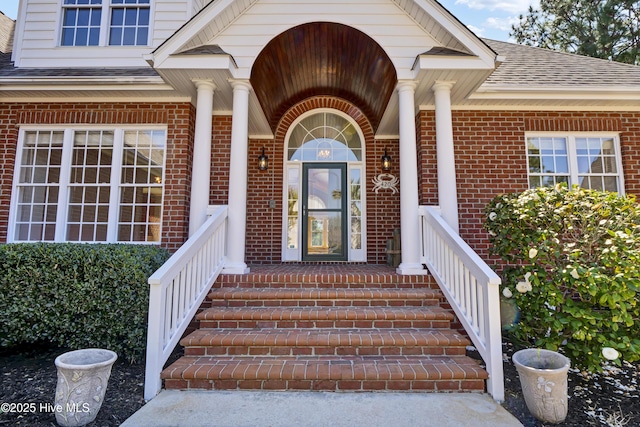 view of exterior entry with brick siding and a shingled roof