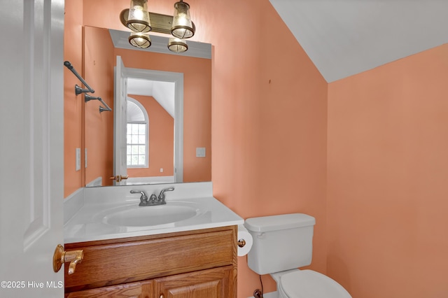 half bathroom featuring toilet, vanity, and vaulted ceiling