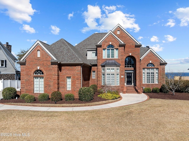 traditional-style home with brick siding, roof with shingles, a front lawn, and fence