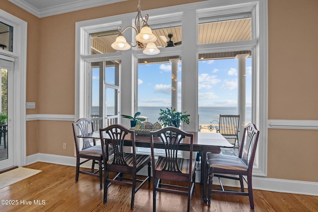 dining room featuring an inviting chandelier, crown molding, wood finished floors, and a water view