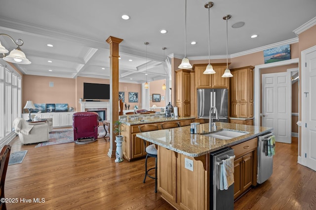 kitchen featuring an island with sink, brown cabinets, wood finished floors, stainless steel appliances, and a sink