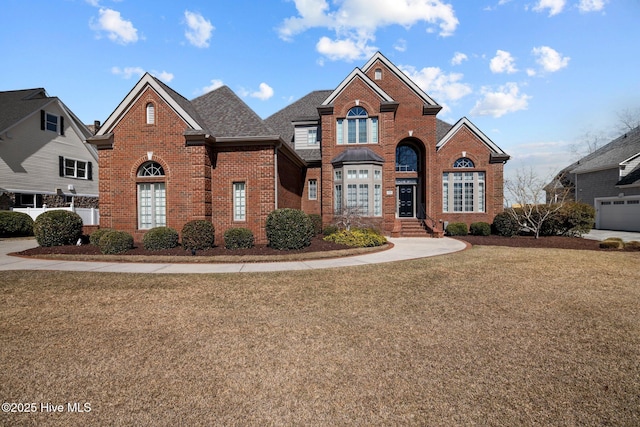 traditional home with brick siding, a front yard, and roof with shingles