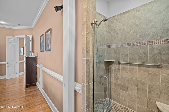 bathroom featuring crown molding, wood finished floors, baseboards, and a shower stall