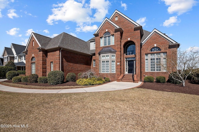 traditional home with brick siding, roof with shingles, and a front yard