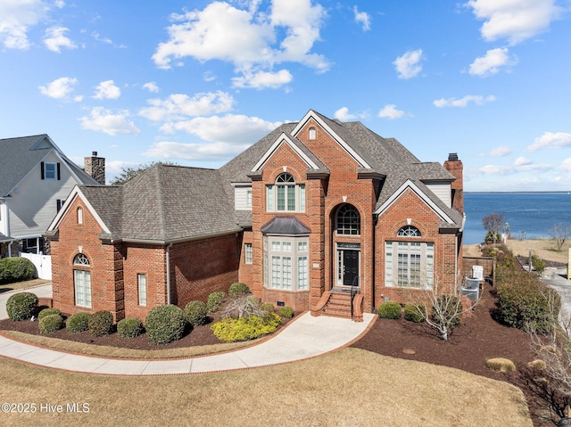 traditional-style home with brick siding, a chimney, and a shingled roof