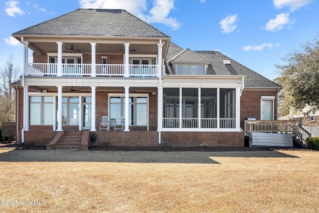 rear view of property featuring a balcony, a ceiling fan, a sunroom, a lawn, and brick siding