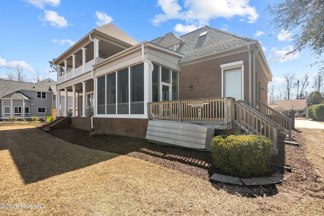 rear view of house with brick siding, roof with shingles, and a sunroom