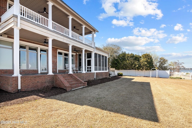 rear view of property with a balcony, fence, a sunroom, brick siding, and ceiling fan