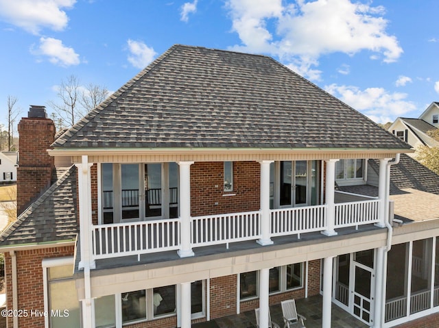 rear view of property featuring brick siding, a chimney, and a shingled roof