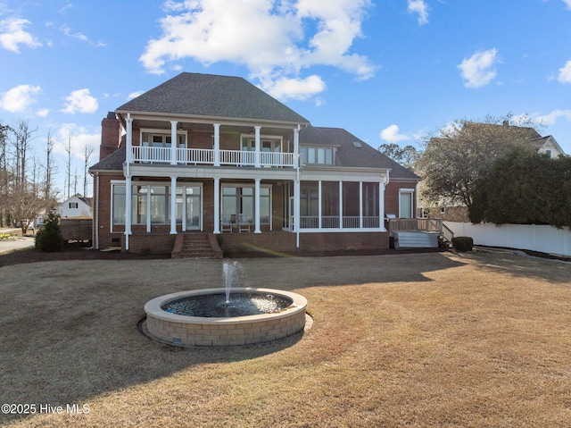 back of property with a balcony, a yard, a sunroom, a chimney, and brick siding