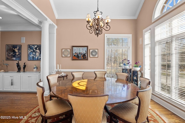 dining area featuring decorative columns, wood finished floors, a notable chandelier, and ornamental molding