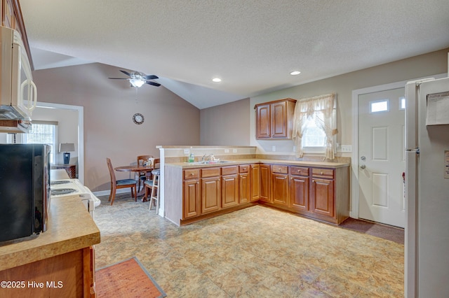 kitchen featuring brown cabinets, white appliances, a peninsula, light countertops, and vaulted ceiling