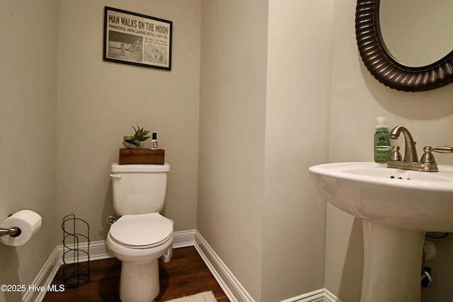 half bathroom featuring toilet, wood finished floors, baseboards, and a sink