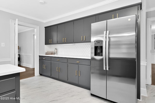 kitchen with gray cabinetry, crown molding, stainless steel fridge with ice dispenser, light countertops, and decorative backsplash