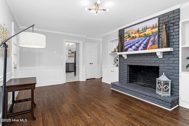 unfurnished living room featuring built in features, wood finished floors, wainscoting, crown molding, and a brick fireplace