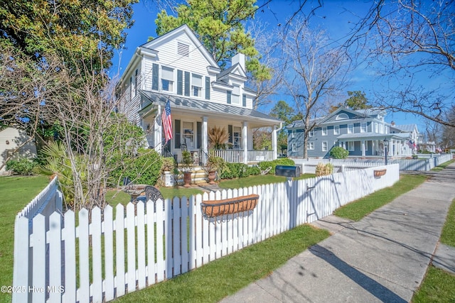 view of front of property with a standing seam roof, a fenced front yard, covered porch, metal roof, and a chimney