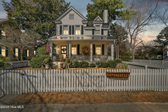 victorian house with a porch, a fenced front yard, and a chimney