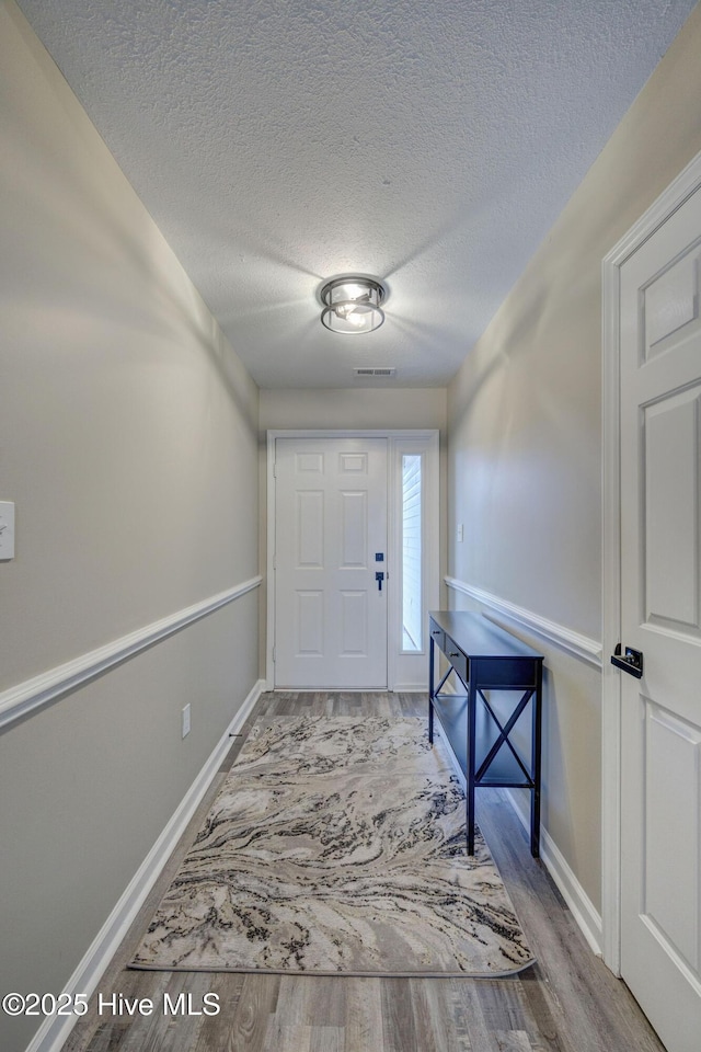 foyer featuring baseboards, wood finished floors, visible vents, and a textured ceiling