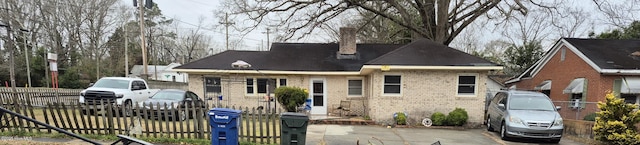 view of front facade with brick siding, a chimney, and fence