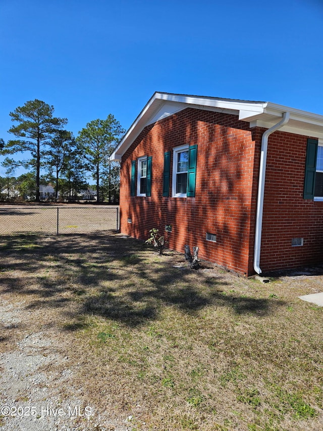 view of side of home with crawl space, a lawn, brick siding, and fence