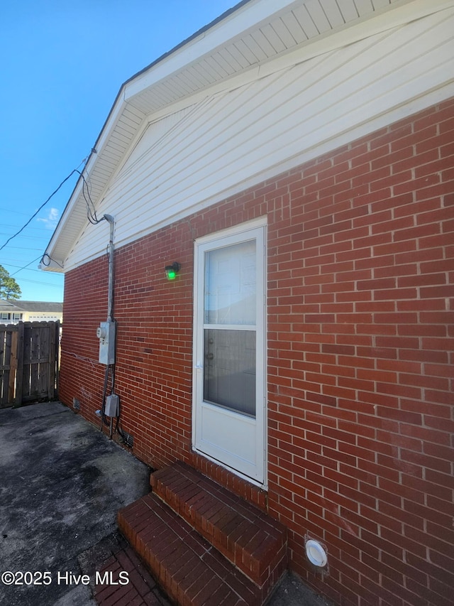 view of side of home featuring entry steps, fence, and brick siding