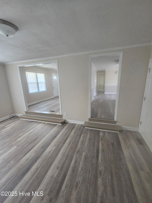 spare room featuring ornamental molding, a textured ceiling, baseboards, and wood finished floors