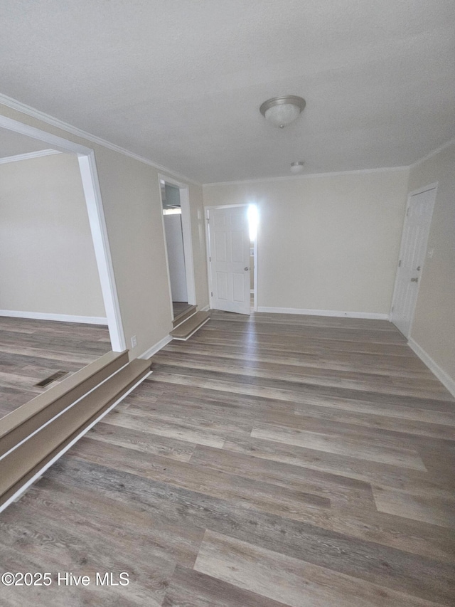 empty room featuring wood finished floors, baseboards, and ornamental molding