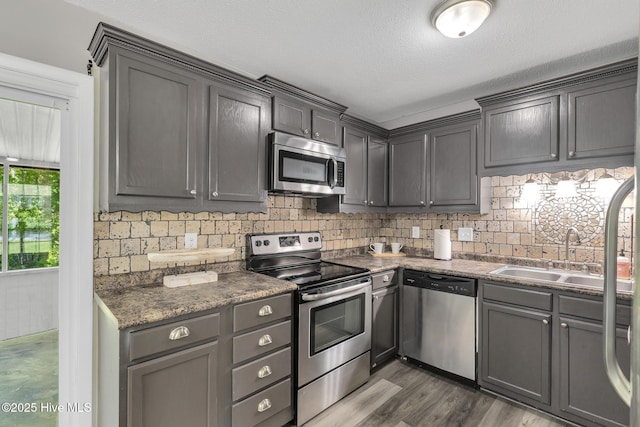 kitchen featuring dark wood-style flooring, dark countertops, appliances with stainless steel finishes, a sink, and tasteful backsplash