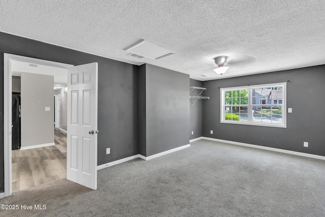 unfurnished room featuring visible vents, baseboards, attic access, a textured ceiling, and carpet