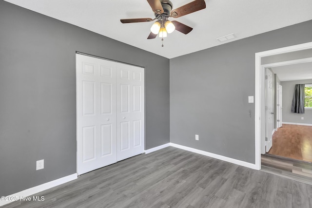 unfurnished bedroom with visible vents, a closet, wood finished floors, baseboards, and a ceiling fan