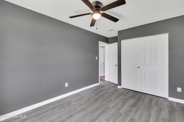 unfurnished bedroom with a ceiling fan, visible vents, wood finished floors, baseboards, and a closet