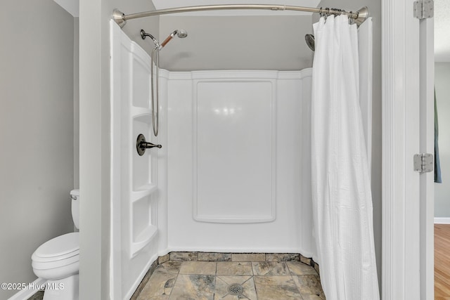 bathroom featuring stone finish floor, baseboards, toilet, and a shower with shower curtain