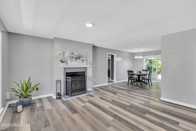 living room with a textured ceiling, a fireplace, wood finished floors, baseboards, and a chandelier