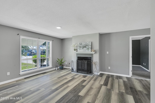 unfurnished living room with baseboards, a fireplace with raised hearth, a textured ceiling, and wood finished floors