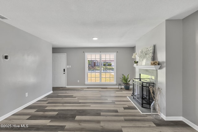 unfurnished living room with a textured ceiling, baseboards, and wood finished floors