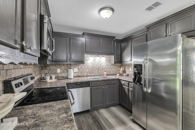 kitchen with appliances with stainless steel finishes, a sink, decorative backsplash, wood finished floors, and visible vents