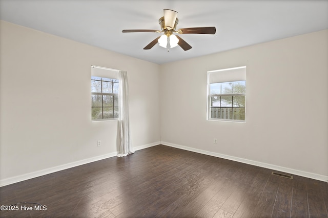 empty room featuring a wealth of natural light, visible vents, baseboards, and dark wood-type flooring