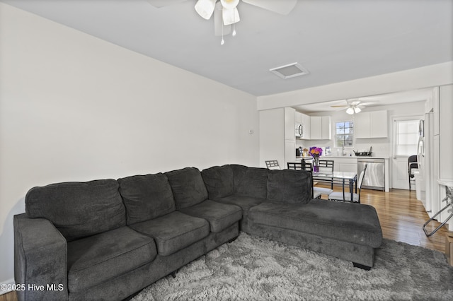 living area featuring visible vents, light wood-style flooring, attic access, and a ceiling fan