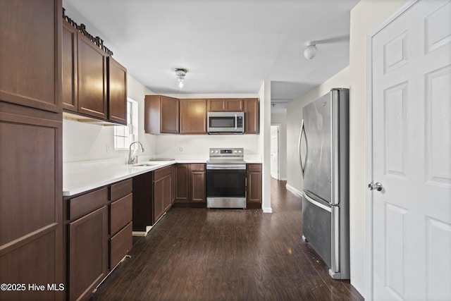 kitchen with baseboards, dark wood finished floors, light countertops, stainless steel appliances, and a sink